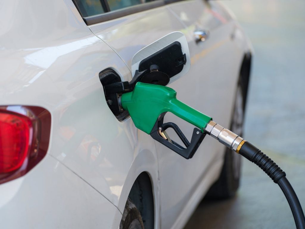 pexels-photo-12377482 Close-up of a green nozzle refueling a white car at a gas station.
